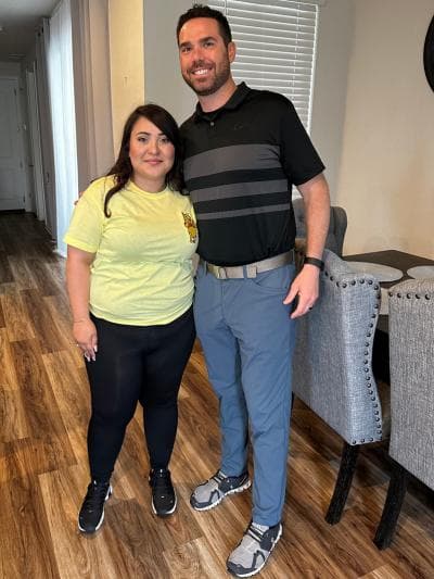 Brendan McQuaid beside a client in a yellow tee, indoors on a wood floor