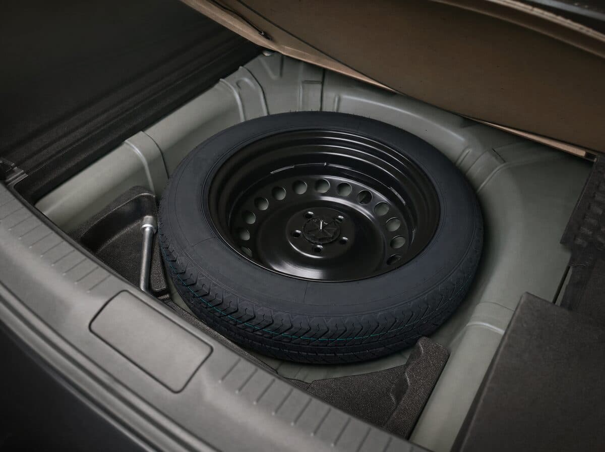 A never-used spare tire in the trunk well of a car, the floor panel lifted